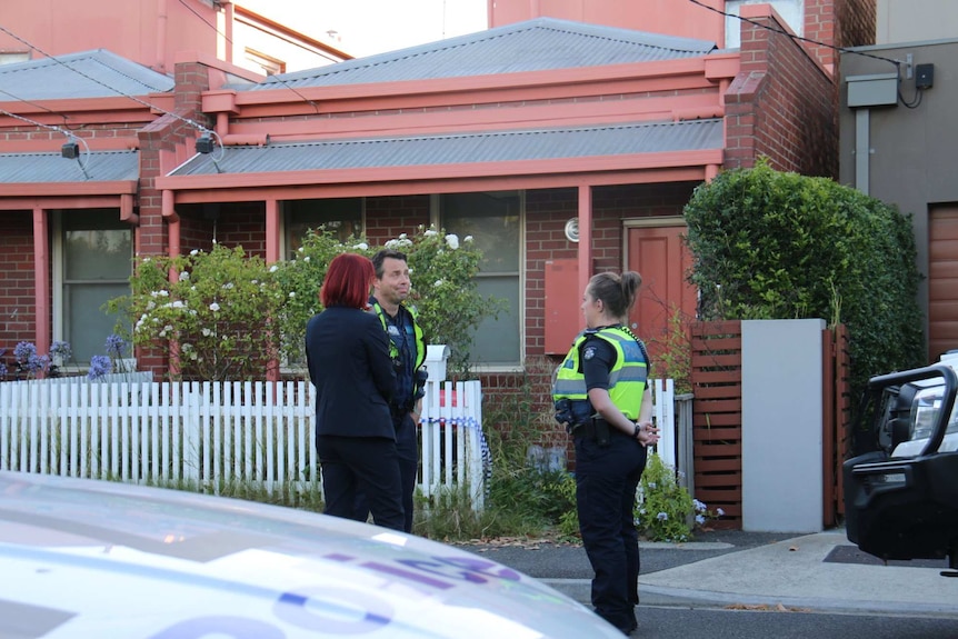 Several police officers stand outside a house.