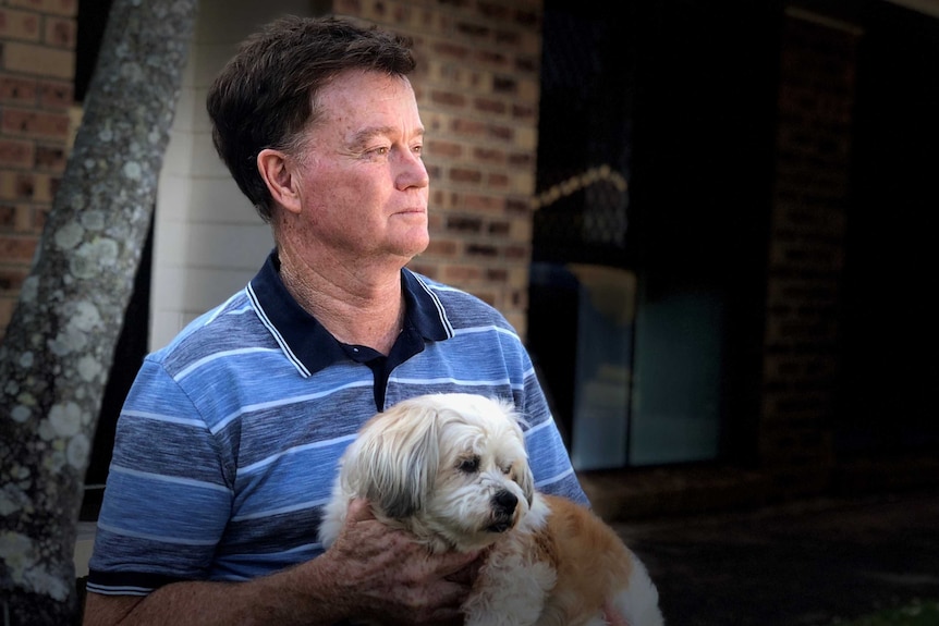 Paul Quirk holds his small dog while looking off into the distance.
