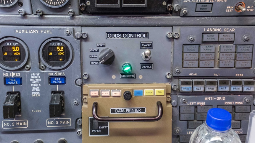 An aeroplane control panel with dials and switches. In the centre shines a green light marked "URD open".