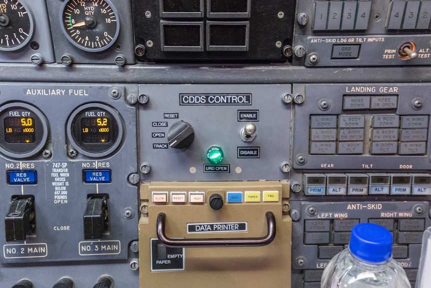An aeroplane control panel with dials and switches. In the centre shines a green light marked "URD open".