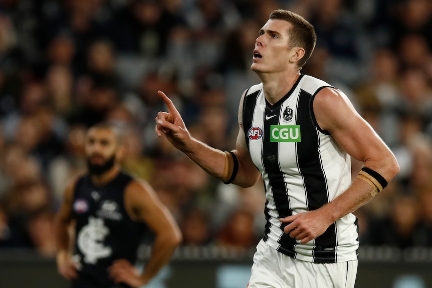 A Collingwood AFL player points a finger on his right hand after kicking a goal against Carlton.