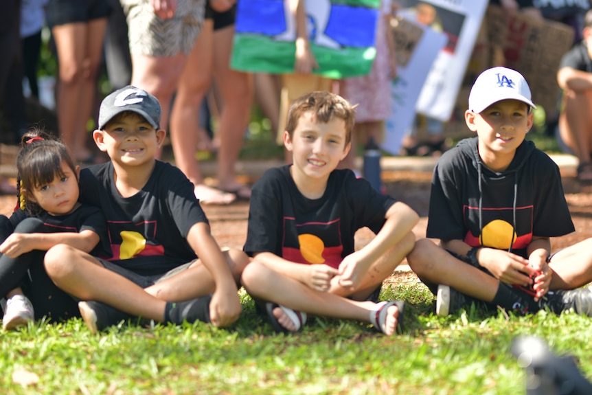 Four kids wearing Aboriginal flag shirts sit together