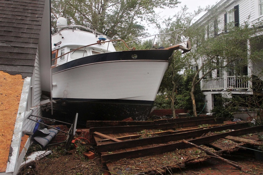 A boat rests between the shifted roof of a garage and a damaged home