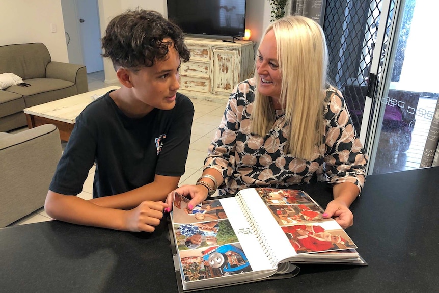 Romeo Paora and his mother Nicky Paora sit at a table with a photo album in front of them.