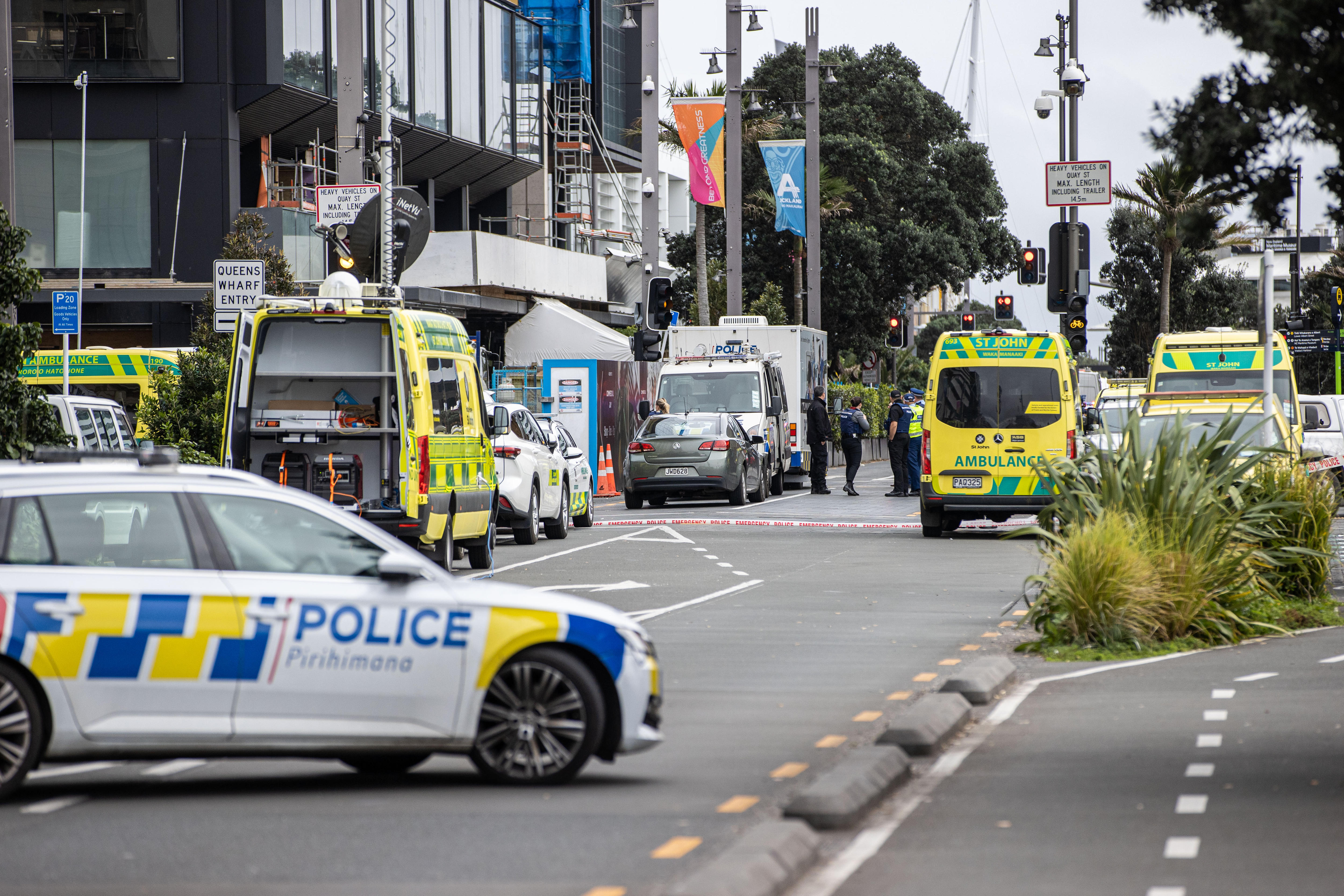 A street with multiple yellow and green ambulances and police cars infront of a building under construction