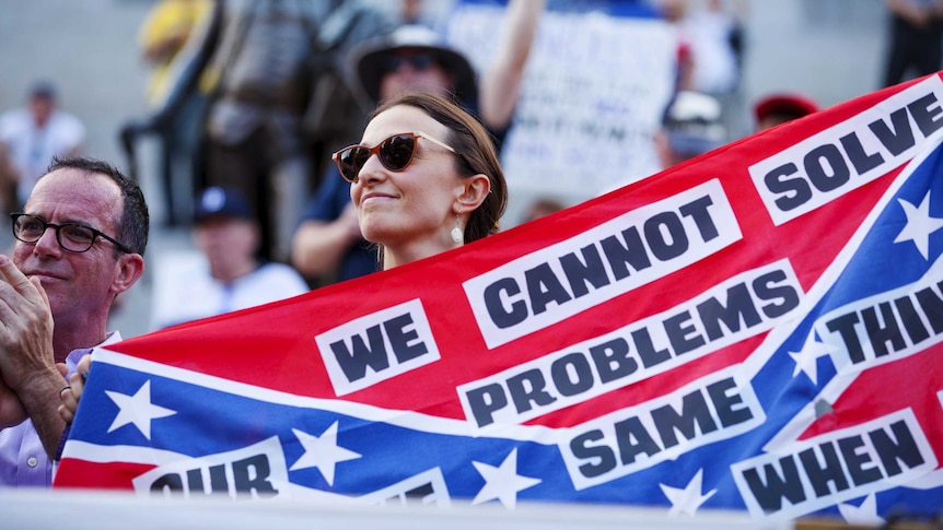 Woman holds banner asking for removal of Confederate flag