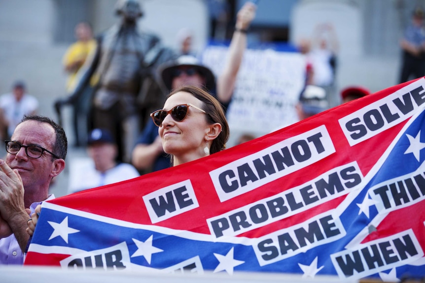 Woman holds banner asking for removal of Confederate flag