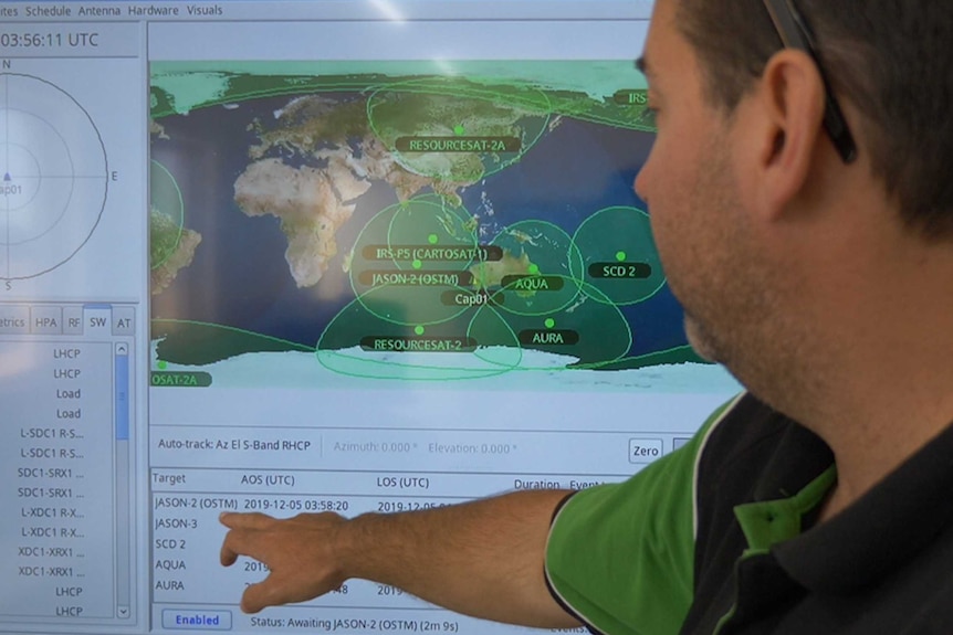 A man points at a screen showing satellite tracking data.