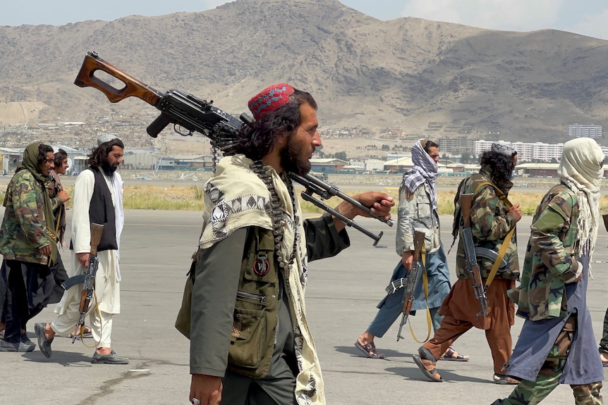 A man with a gun over his shoulder walking on an airport runway.