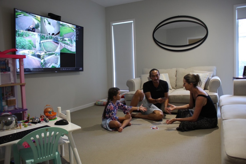 Mum, dad and daughter playing uno in living room with TV showing surveillance vision