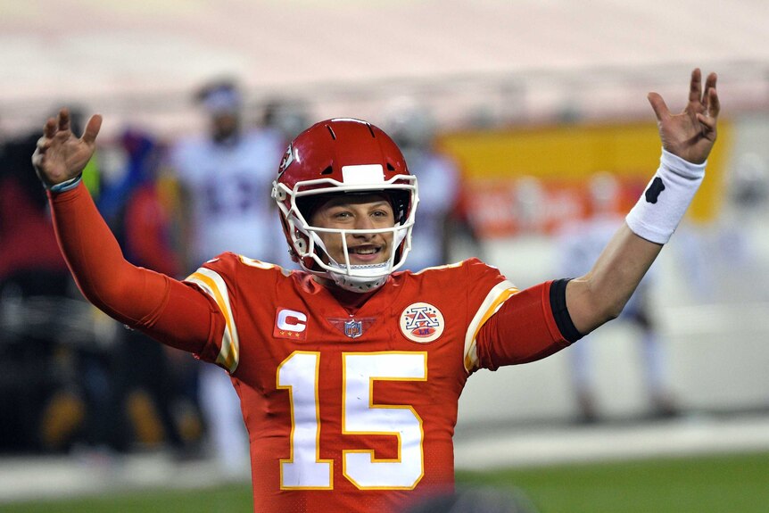 Patrick Mahomes smiles and holds both hands up above his head