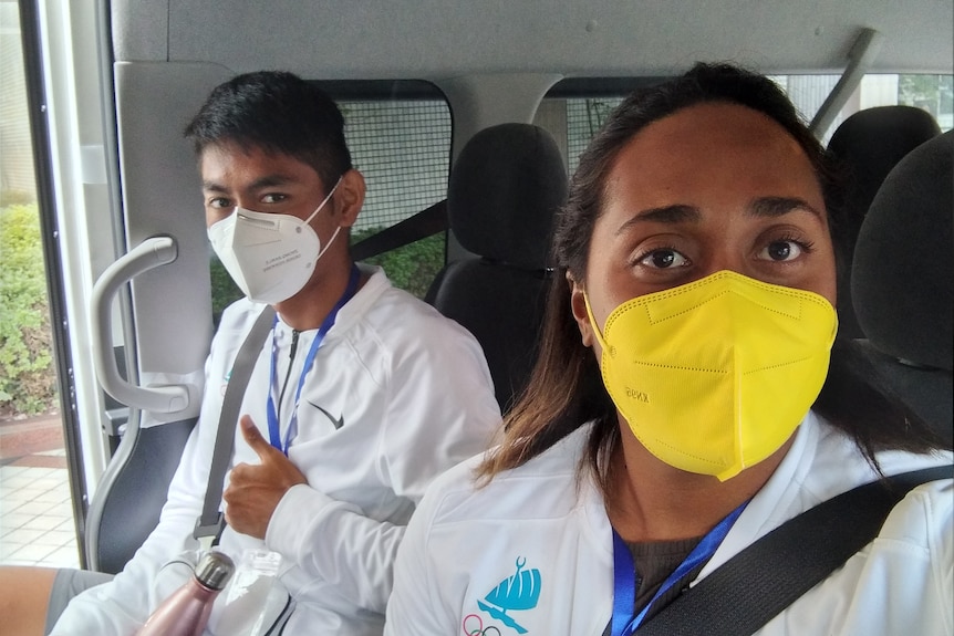 Woman and man wearing masks on bus seats, man gives thumbs up to camera.