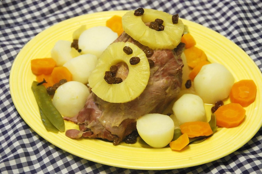 A close up of lamb, vegetables and pineapples on a yellow plate.