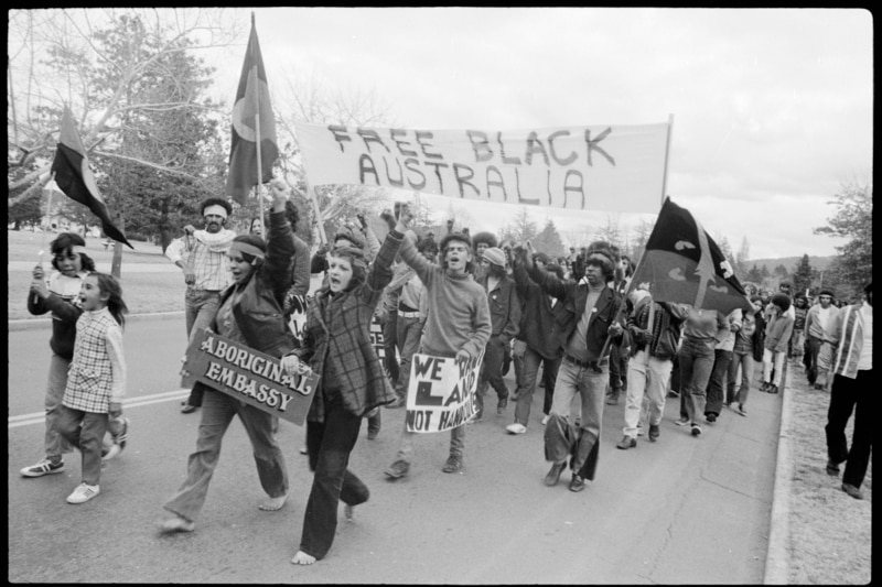 A black and white photo of a group of people protesting on the streets holding a sign that says 'free black australia'