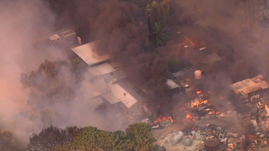 Fire burning in a scrapyard with black smoke rising across other buildings