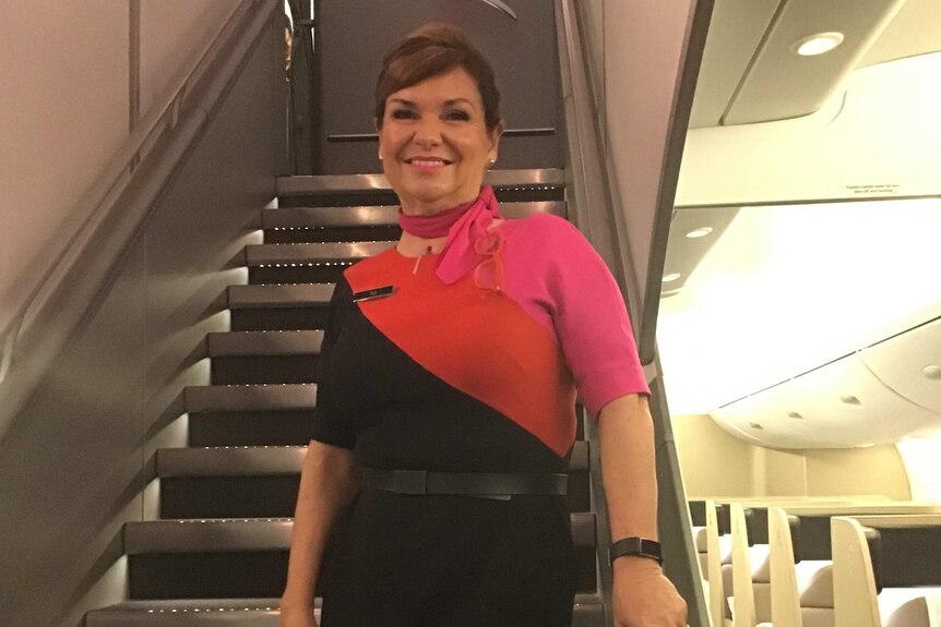 Suzi Hannan in Qantas flight attendant uniform stands at the bottom of internal stair on an aircraft