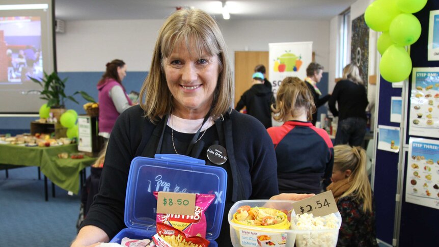 A photo of a lady wearing an apron holding a healthy lunch box and an unhealthy lunch box