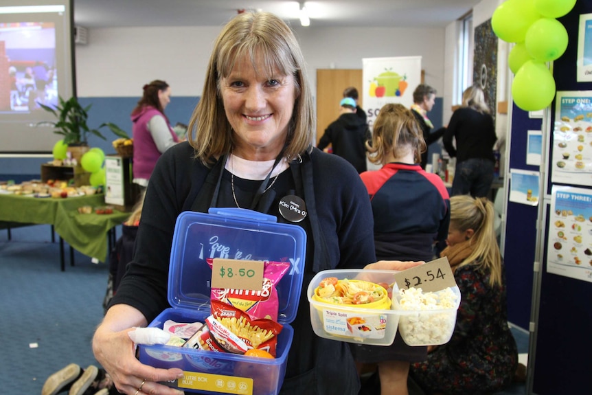 A photo of a lady wearing an apron holding a healthy lunch box and an unhealthy lunch box