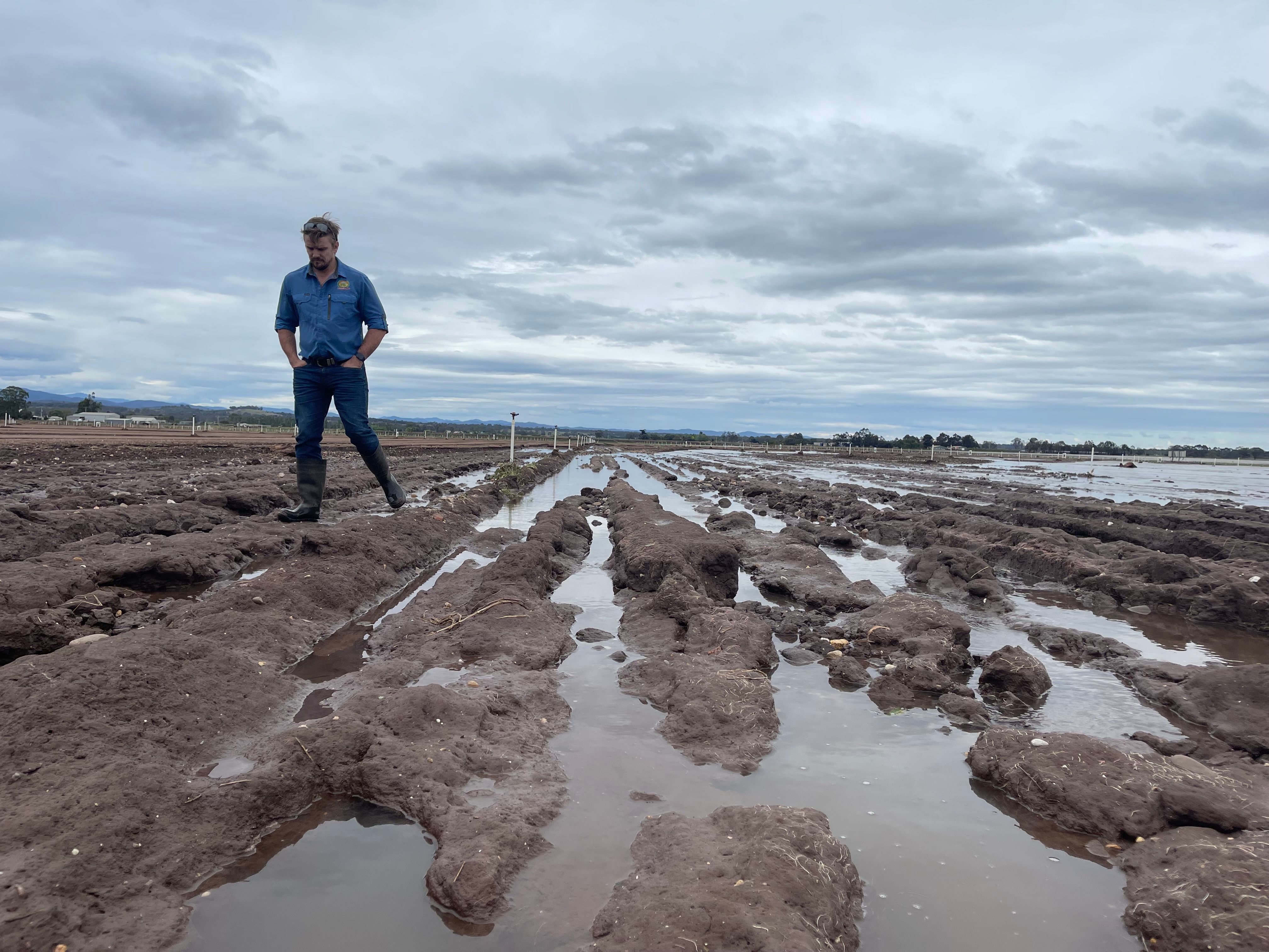 A farmer in a blue shirt and jeans, inspects a damaged field with visible water everywhere