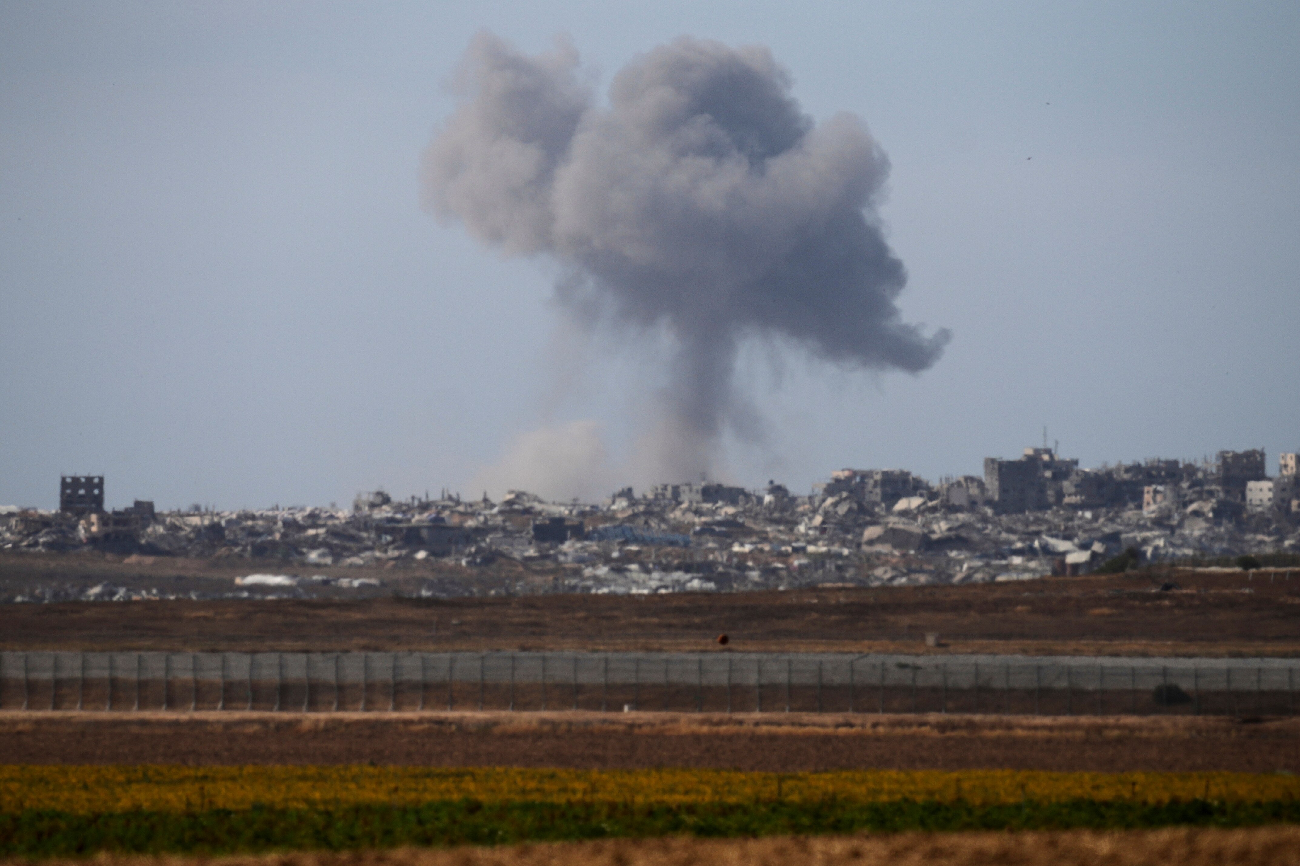 Crumpled buildings sit in across the horizon as a cloud of smoke from a bomb rises into the sky above