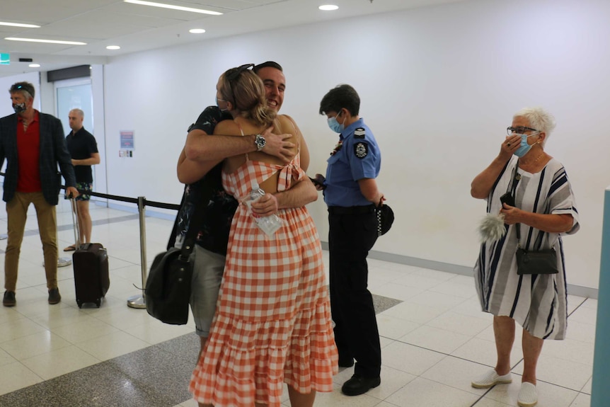 A man and a woman hug in an airport terminal.