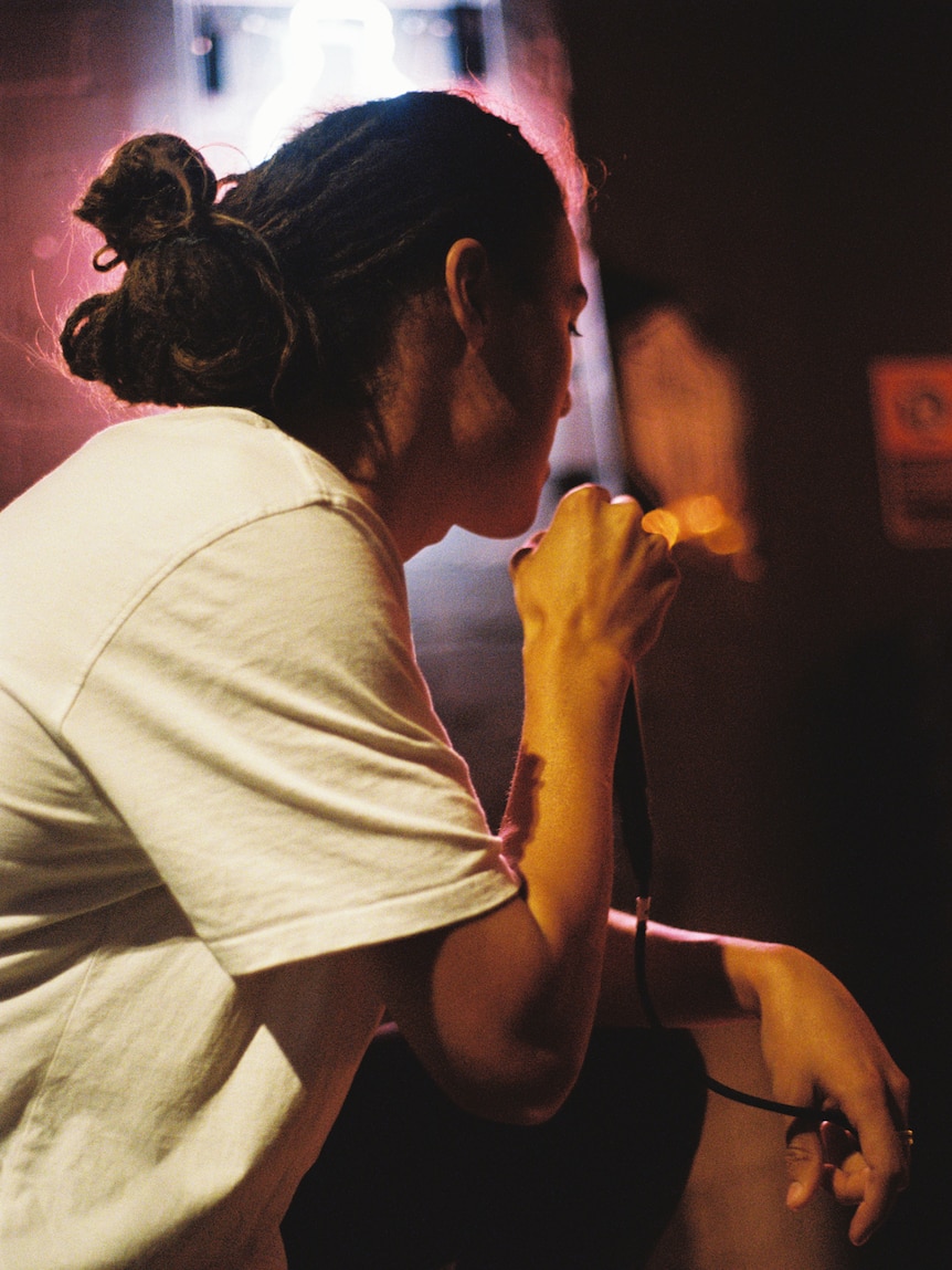 A man sits down on stage, looking away from camera and holding a microphone.