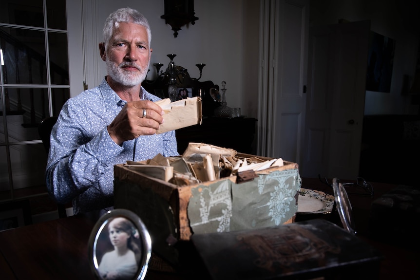 A man with grey hair and a beard holding a letter from a box