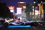 A silver F1 car, at night, on the Las Vegas Strip, driving for specators