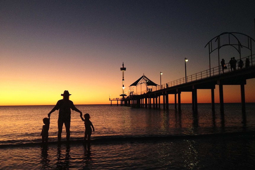 A family play in the shallows at Brighton Beach during sunset.