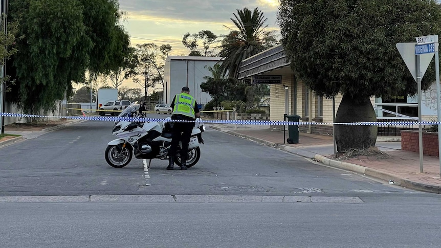 Police tape across a suburban street where a police officer stands next to his motorbike.