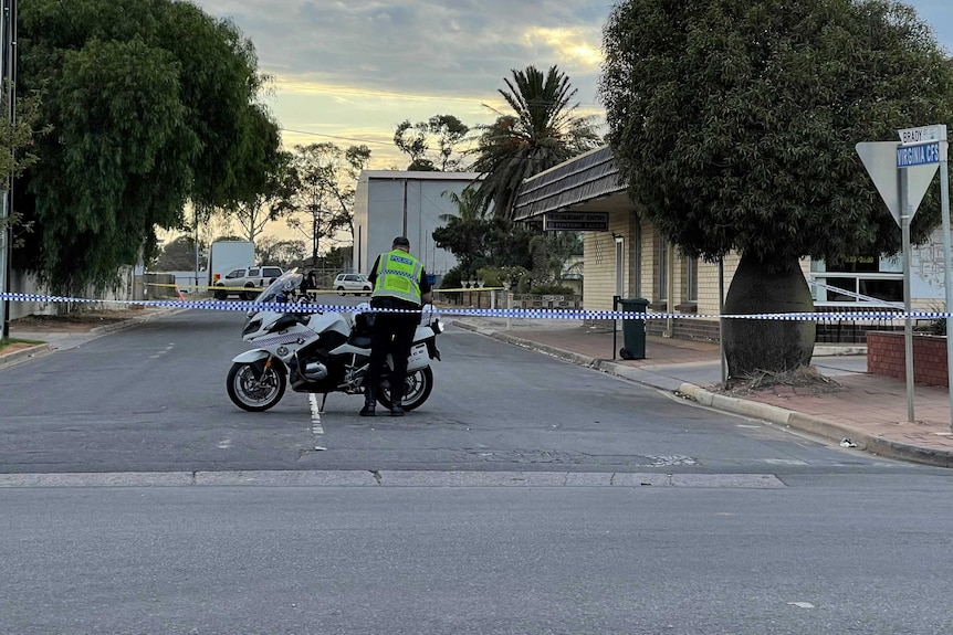 Police tape across a suburban street where a police officer stands next to his motorbike.