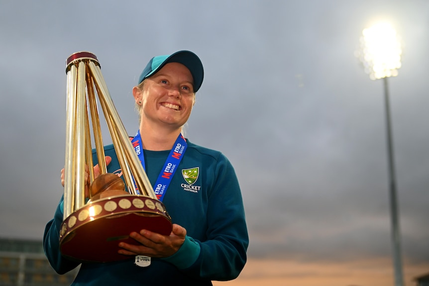 A woman smiles while holding a trophy.