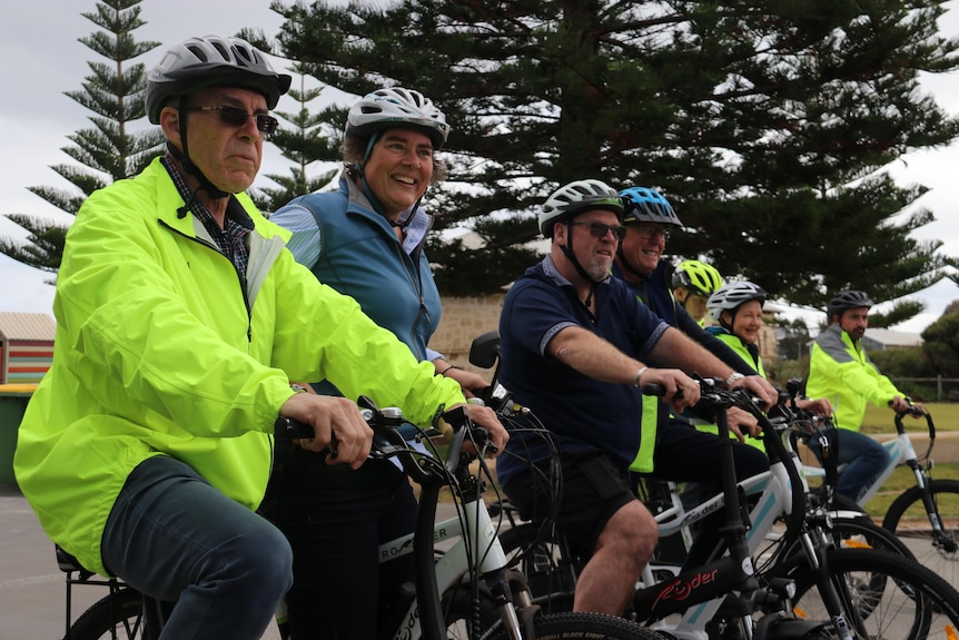 A group of cyclists riding e-bikes lined up in a row