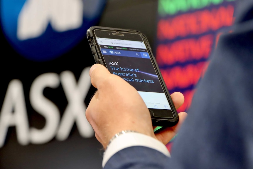 The hand of a man in a suit checking the ASX website on his phone at the ASX.