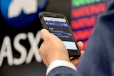 The hand of a man in a suit checking the ASX website on his phone at the ASX.