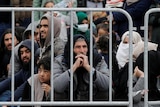 Migrants sitting behind a fence.