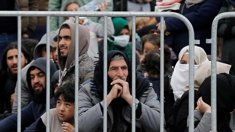 Migrants sitting behind a fence.