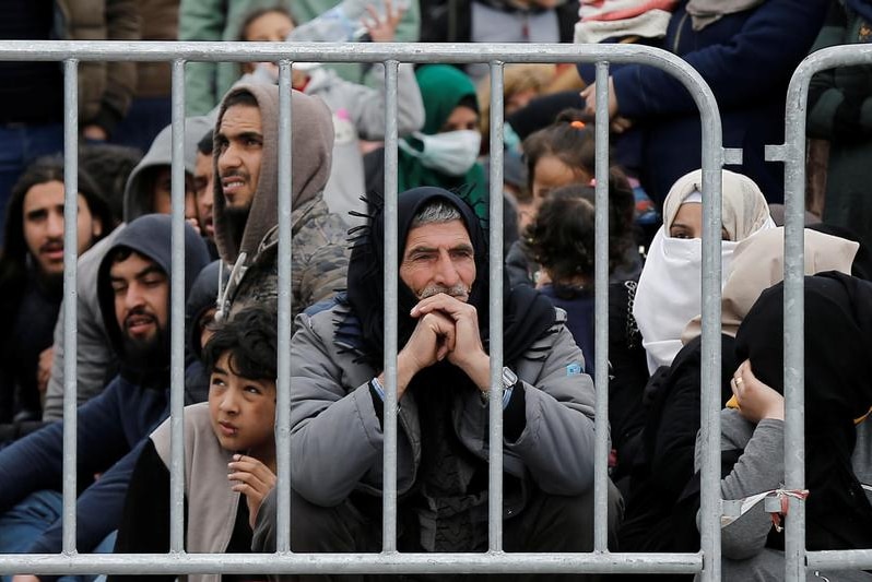 Migrants sitting behind a fence.