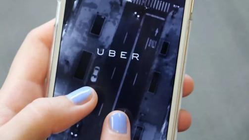 A person with blue nail polish holding a phone with the Uber logo on it