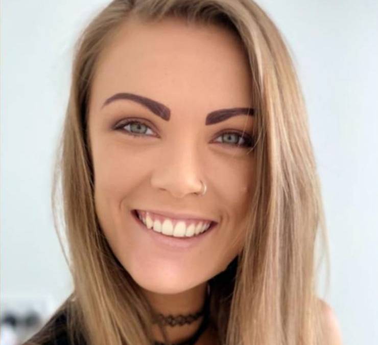 A woman with light brown hair smiles, she has a nose ring.