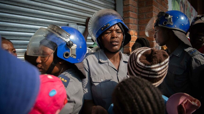 police wearing helmets stand near people queueing outside a store
