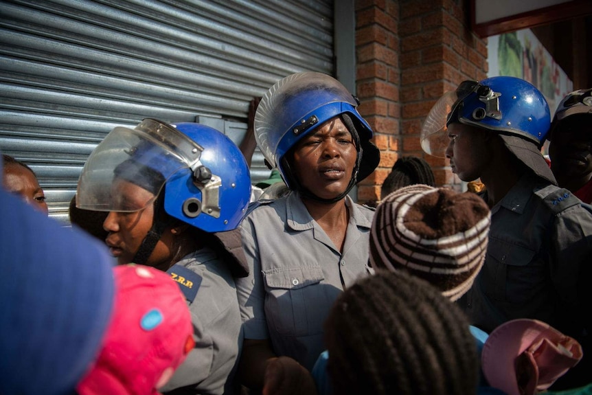 police wearing helmets stand near people queueing outside a store