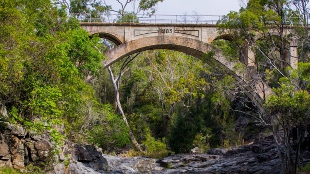 Concrete arched railway bridge crosses small stony creek