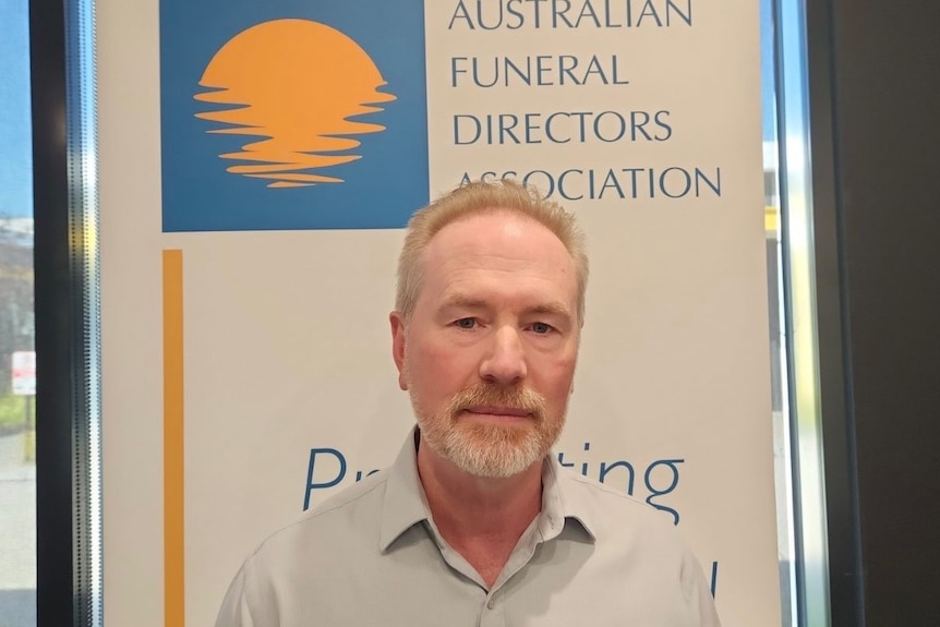 Man looks at camera with sign behind him