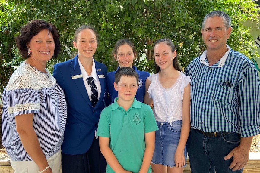 A schoolgirl in uniform smiles alongside three siblings and two parents.