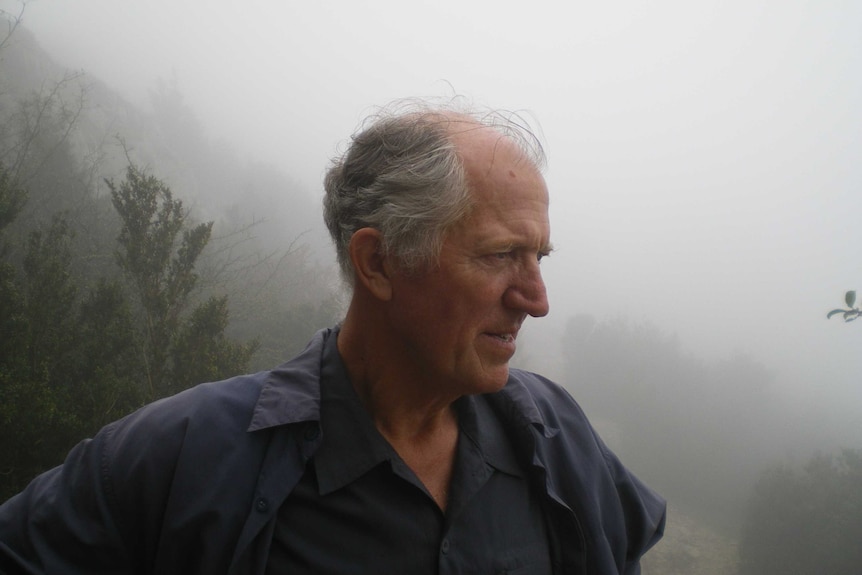 Clive Deverall stands on a mountain surrounded by white mist.