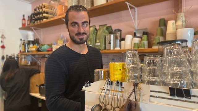 Man stands next to coffee machine stacked with glasses in a cafe.