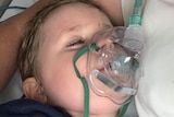 A little boy wearing an oxygen mask in hospital.