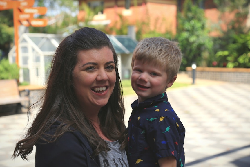 Mother holds her son in an embrace in a courtyard at an aged care facility.