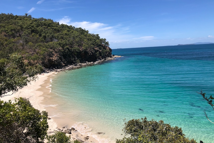 A view of a private beach with sparkling clear blue water on to a white sand beach